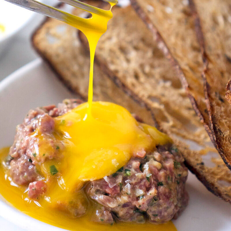 Person breaking the egg on one of the best steak tartare in Seattle