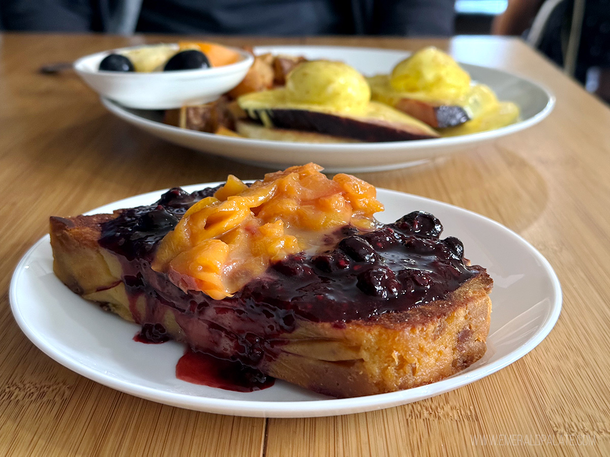 french toast smothered in peach and blueberry compote with an eggs Benedict in the background