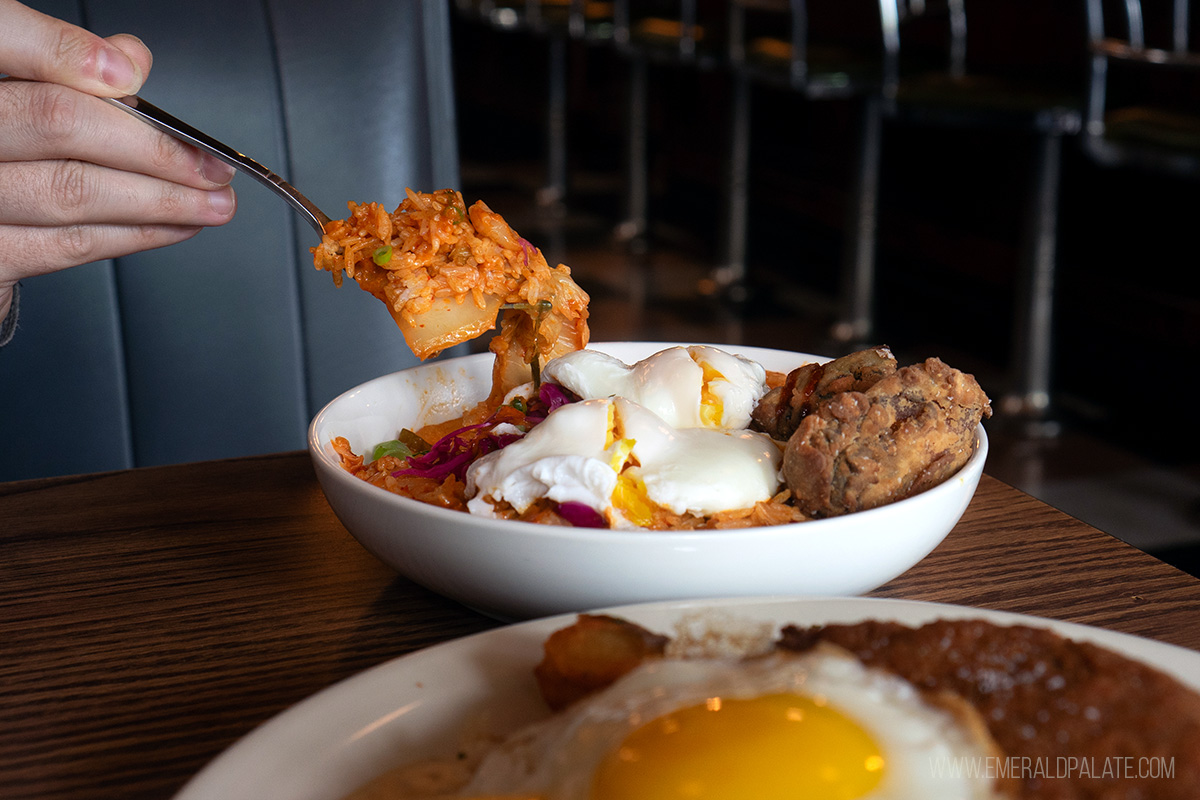 person picking up forkful of kimchi rice bowl with poached egg