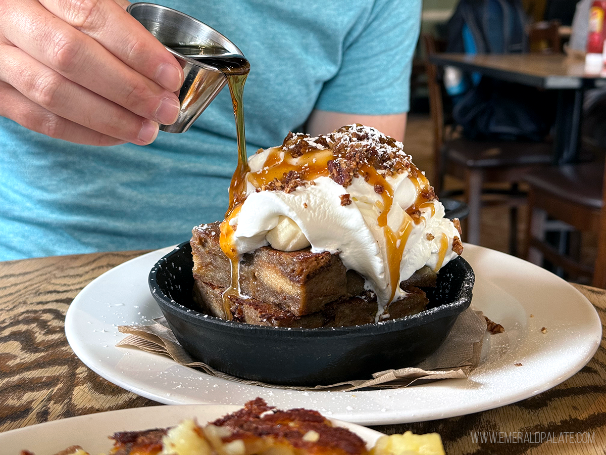 person pouring syrup over French toast smothered in whipped cream