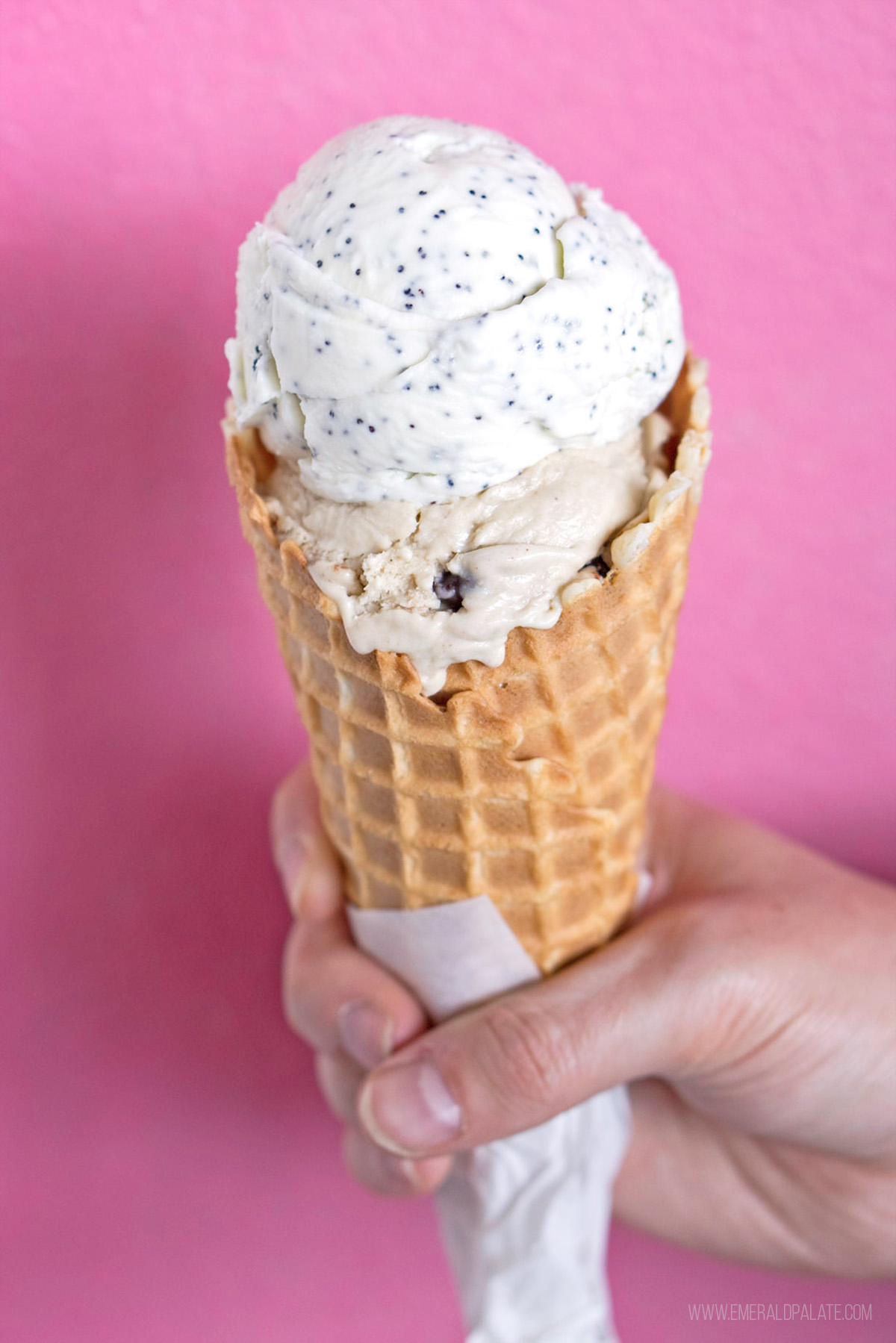 person holding an ice cream cone in front of a pink wall