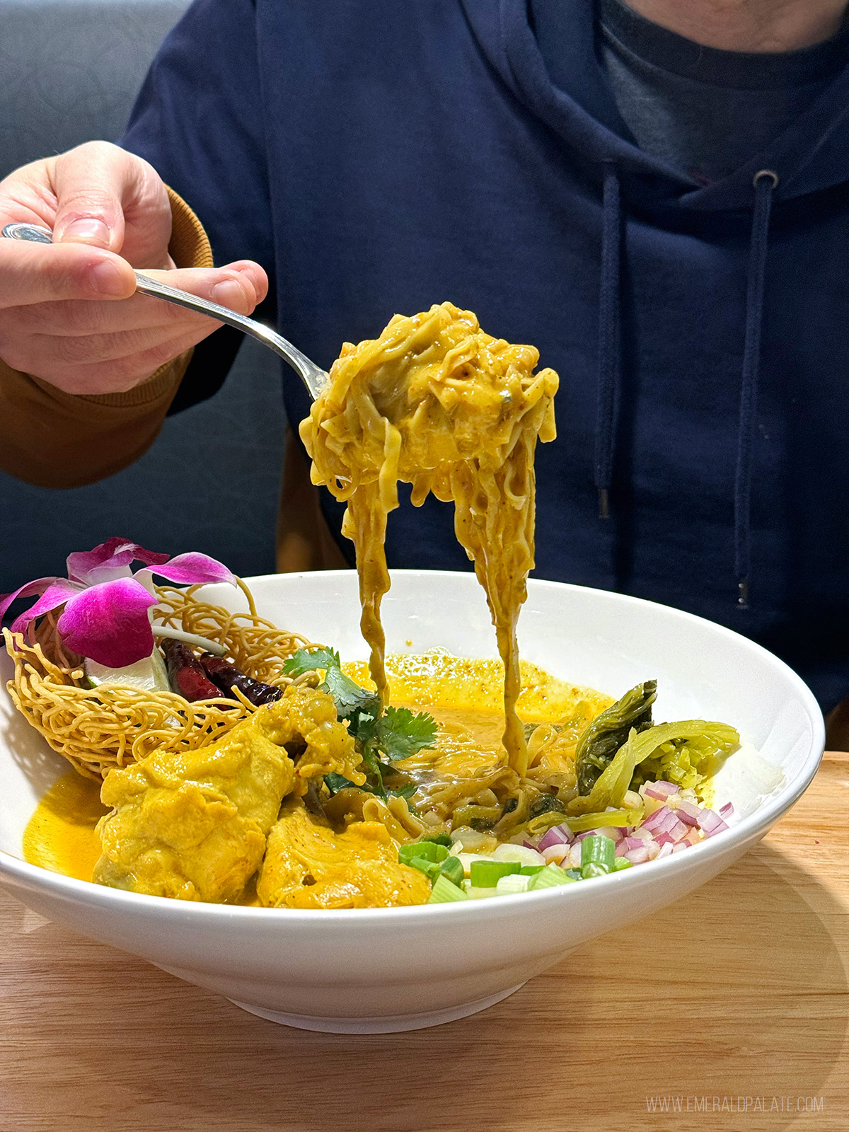 person picking up khao soi curry noodles at one of the best Thai restaurants in Seattle