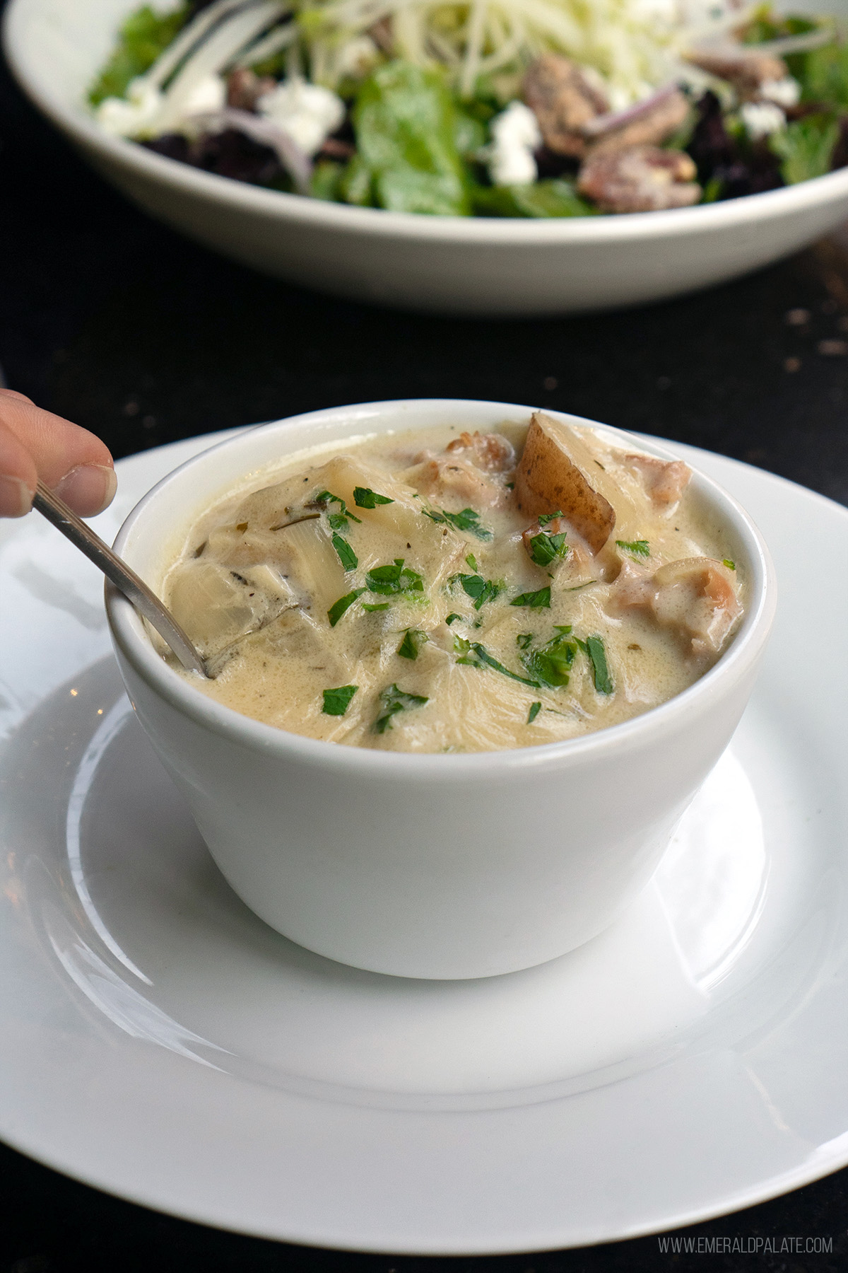 person picking up spoonful of New England clam chowder