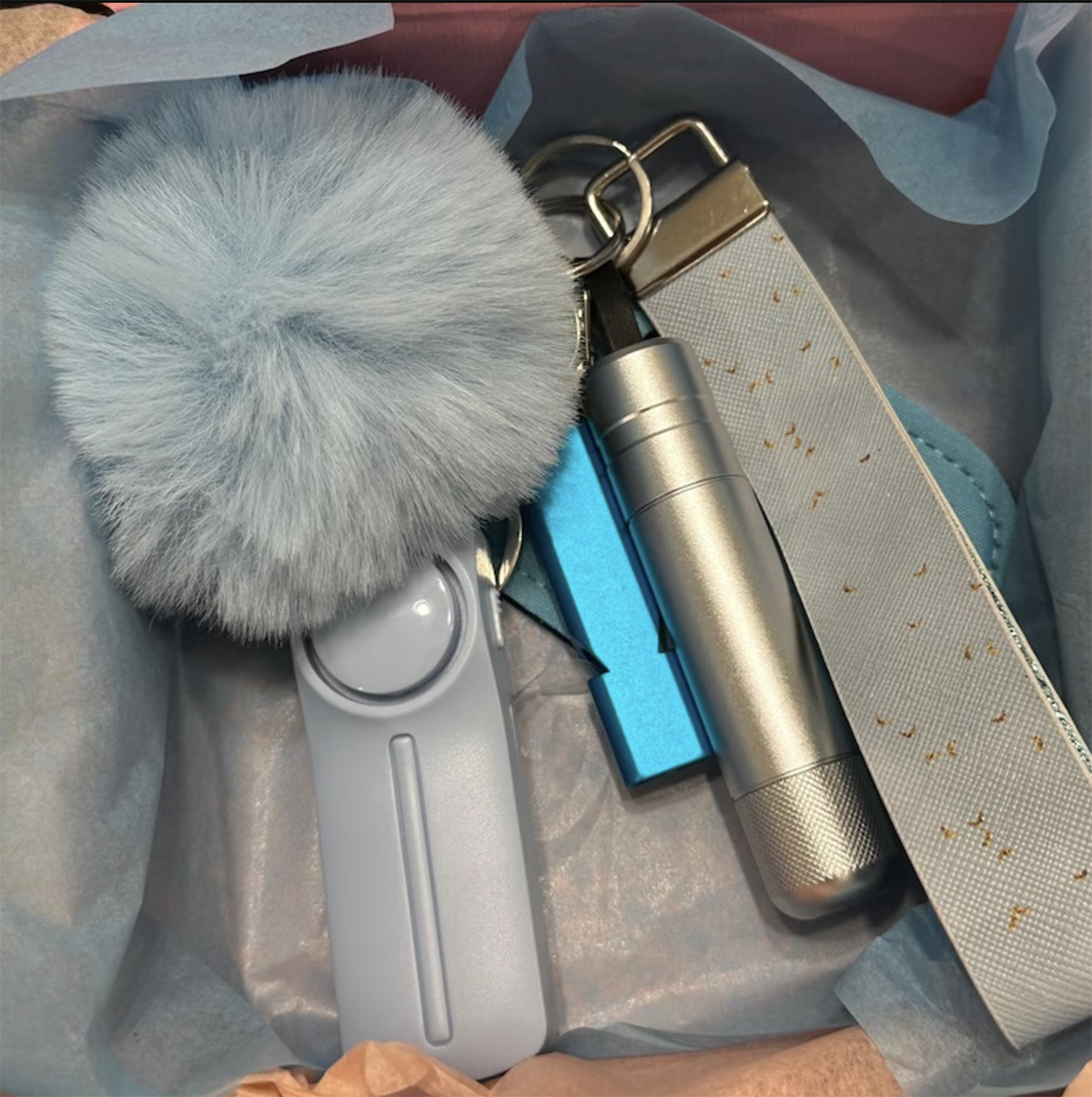 A keychain with a blue pom pom, an alarm, a whistle, a light, and a wristband