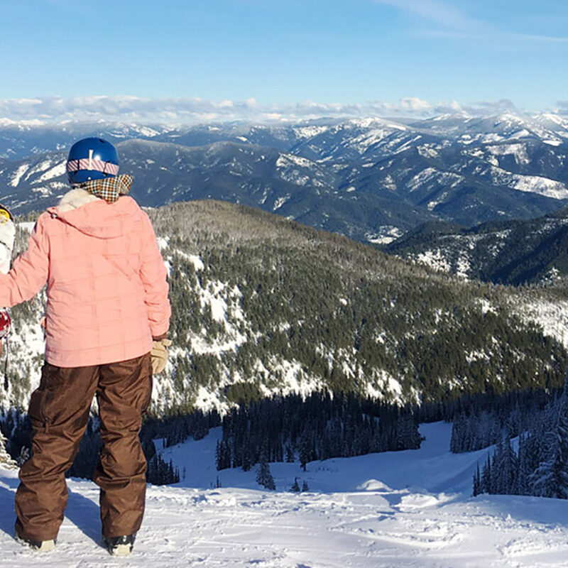 woman looking at mountains in the distance while snowboarding at one of the best ski resorts in Washington