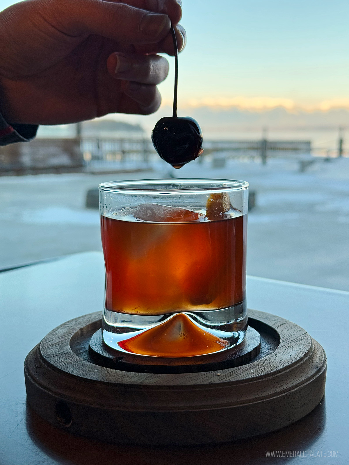 person picking up a cherry from a Manhattan cocktail